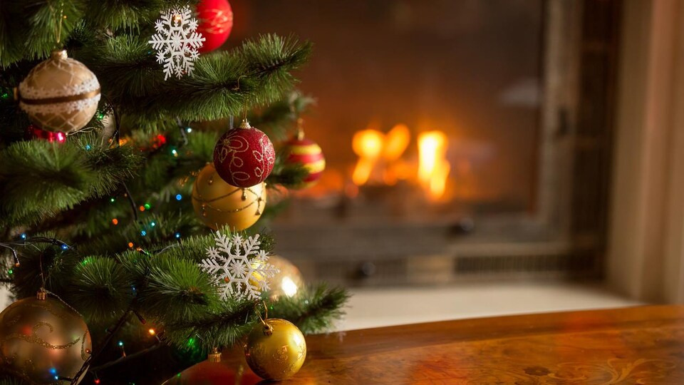 Un arbre de Noël décoré avec des boules rouges et or. Derrière, il y a un feu de foyer.