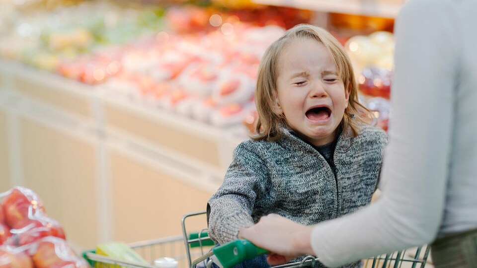 Un jeune enfant dans le chariot pleure fort alors que sa mère essaye de faire son épicerie.
