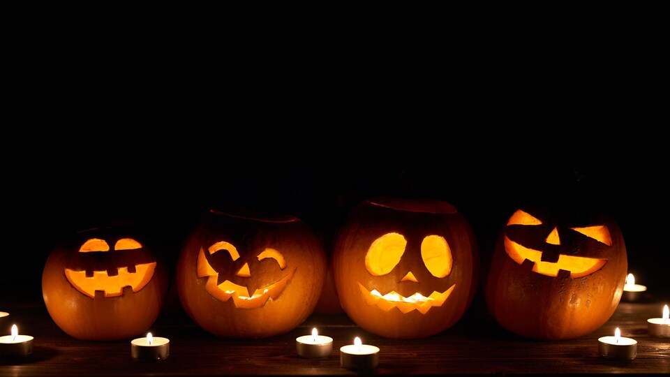 Quatre citrouilles décorées pour l'Halloween sont éclairées par des chandelles dans le noir.