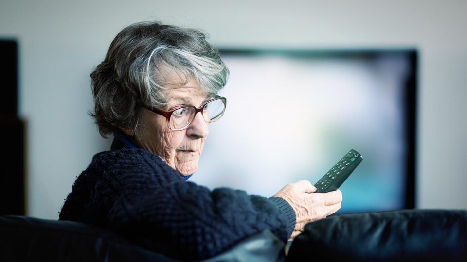 Une femme âgée qui regarde sa télécommande avec surprise. 
