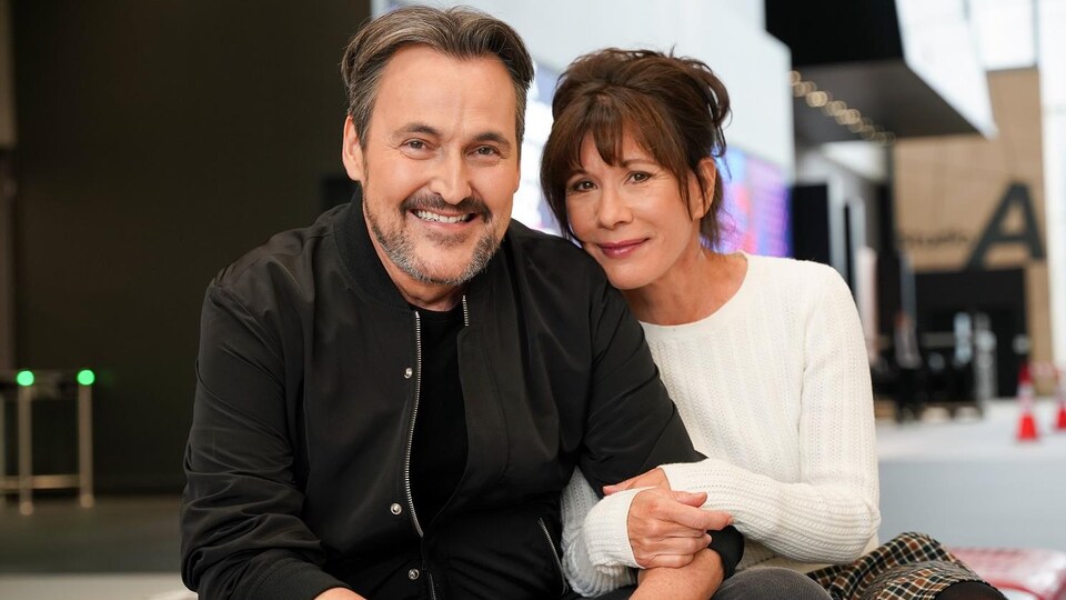 Guy A Lepage et Sylvie Léonard posent, assis, dans l'atrium de la Maison de Radio-Canada.
