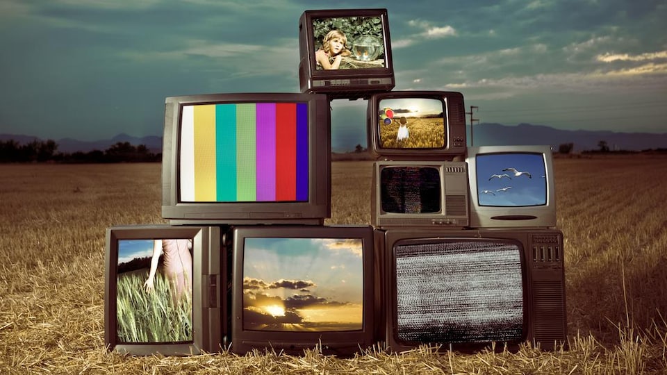 Huit télévisions empilées les unes sur les autres en forme de pyramides dans un champ de blé.