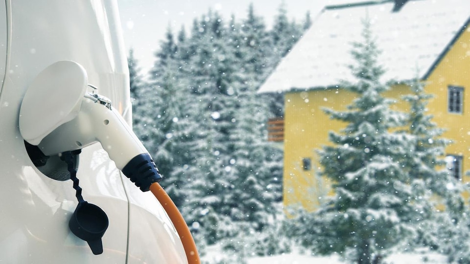 Une voiture électrique branchée à un câble de recharge. C'est l'hiver.