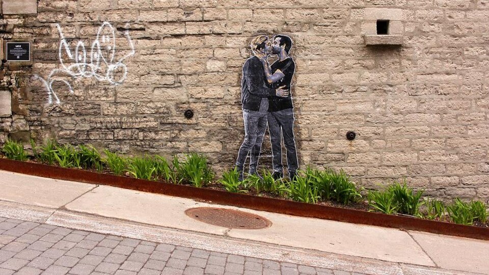 Un collage avec deux hommes qui s'embrassent a été posé sur un mur sur une rue en pente.