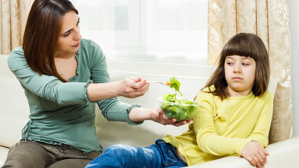Une mère incite sa fille à manger un plat de salade, mais cette dernière n'est pas intéressée à y goûter.