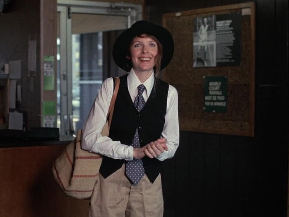 Une femme (Diane Keaton), portant une cravate et un chapeau, sourit.
