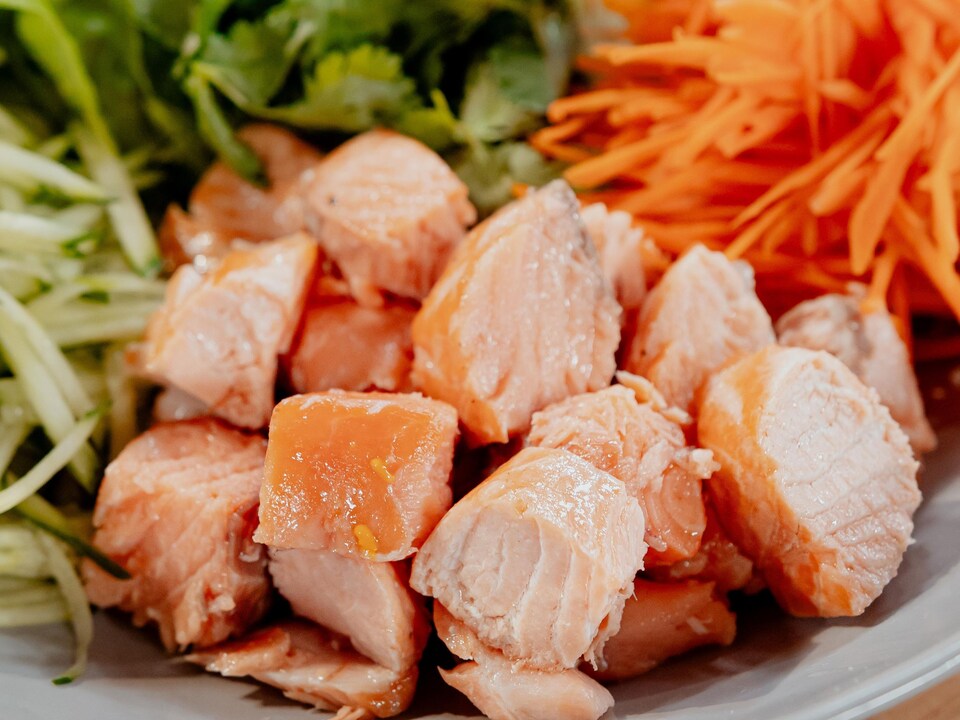 Des cubes de saumon dans une assiette avec des concombres et carottes en julienne.