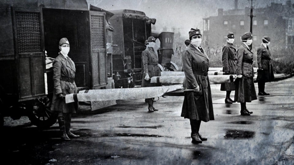 Huit femmes, vêtues en uniforme de l'armée et portant un masque en tissus blanc sur le nez et la bouche, transportent des civières vides.