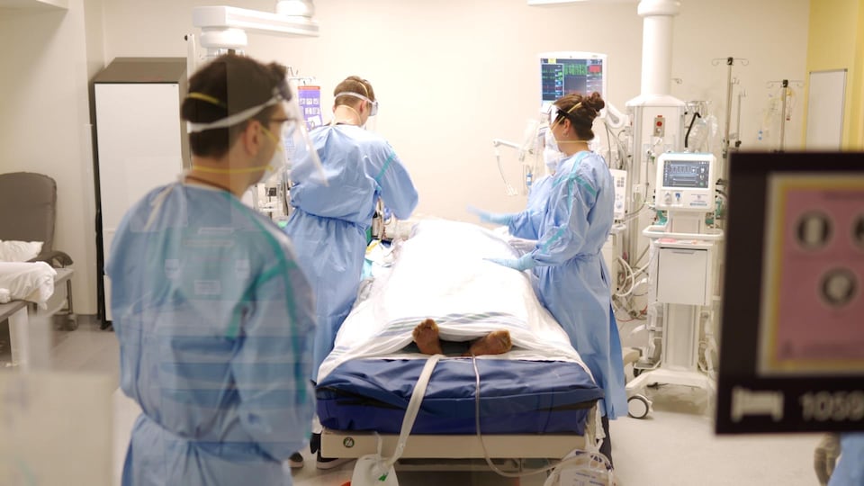Trois personnes du personnel soignant autour d'un lit d'hôpital contenant un malade.