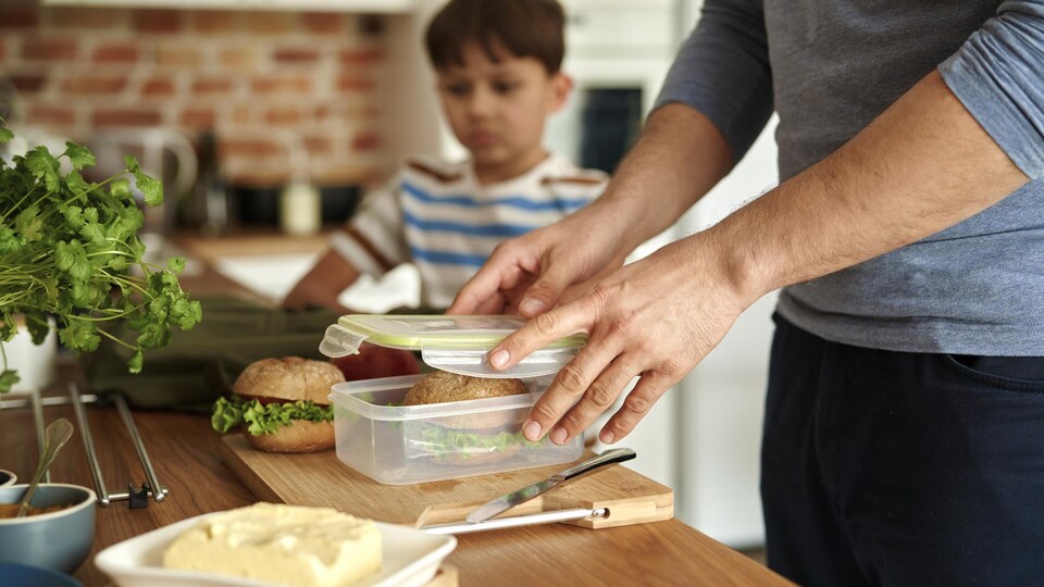 Gros plan sur un père faisant une boîte à lunch contenant un sandwich pour son fils.
