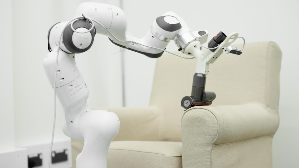 Un bras robotisé passe l'aspirateur sur un fauteuil.