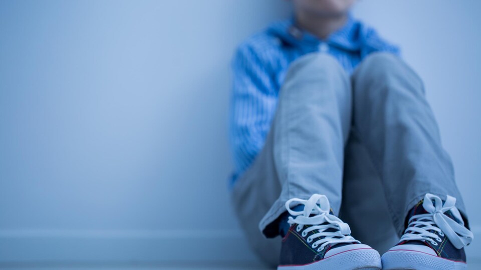 Un garçon à l'air triste est assis, seul, par terre.