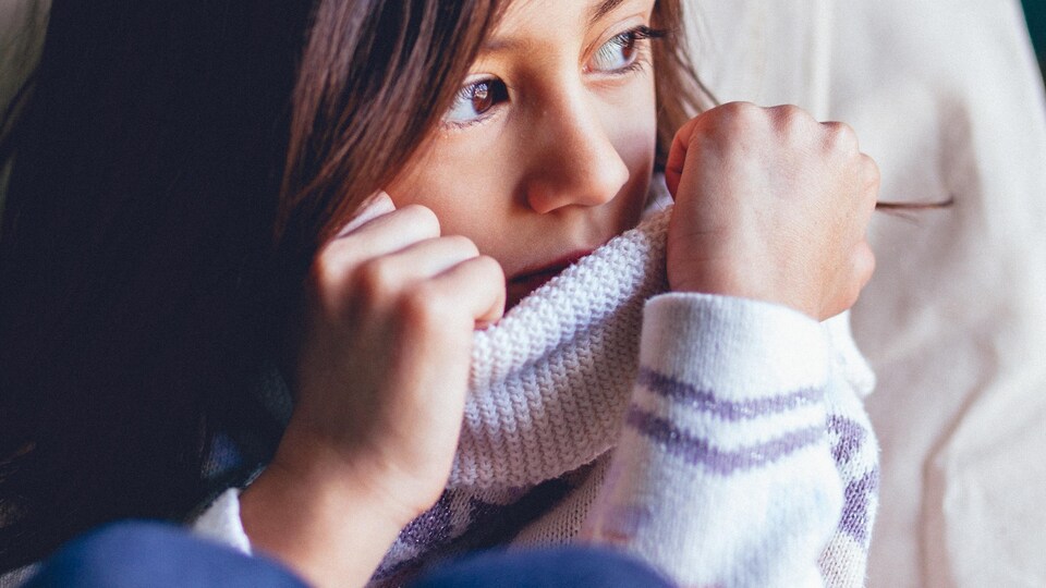 Une petite fille à l'air préoccupé est assise, seule, par terre.