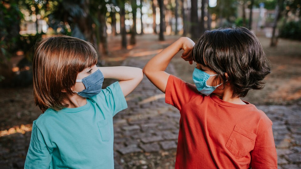 Deux enfants se saluent avec avec le coude et portent un masque.