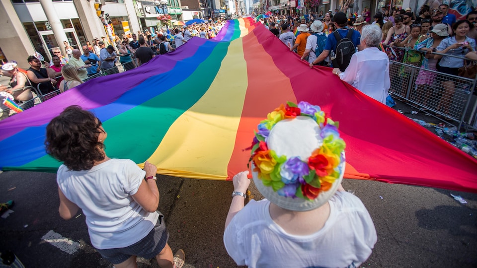 Plusieurs personnes tiennent un drapeau arc-en-ciel LGBT dans un défilé à Toronto.