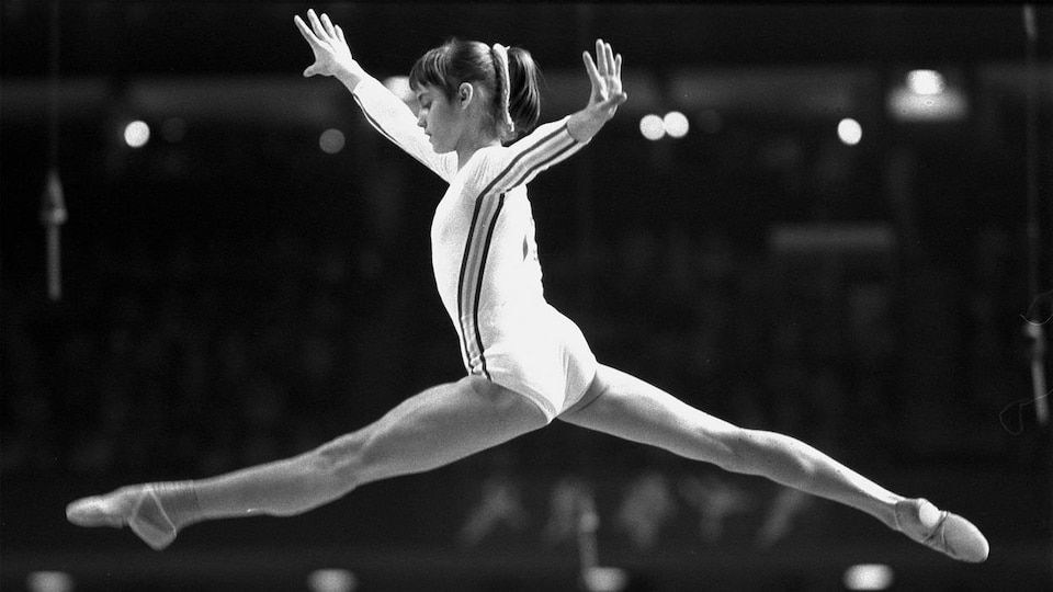 La gymnaste Nadia Comaneci saute en faisant le grand écart.