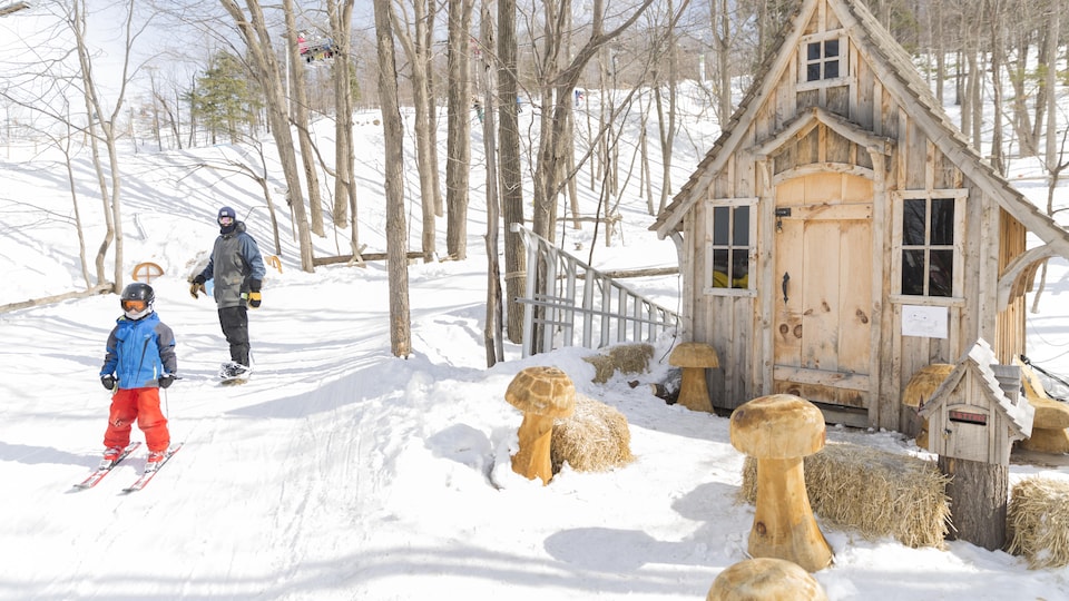 Un enfant skie et un adulte fait de la planche à neige dans la forêt.