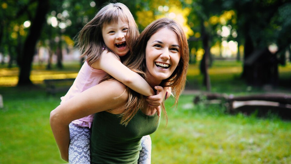 Elles rient dans un parc, la petite fille est trisomique.