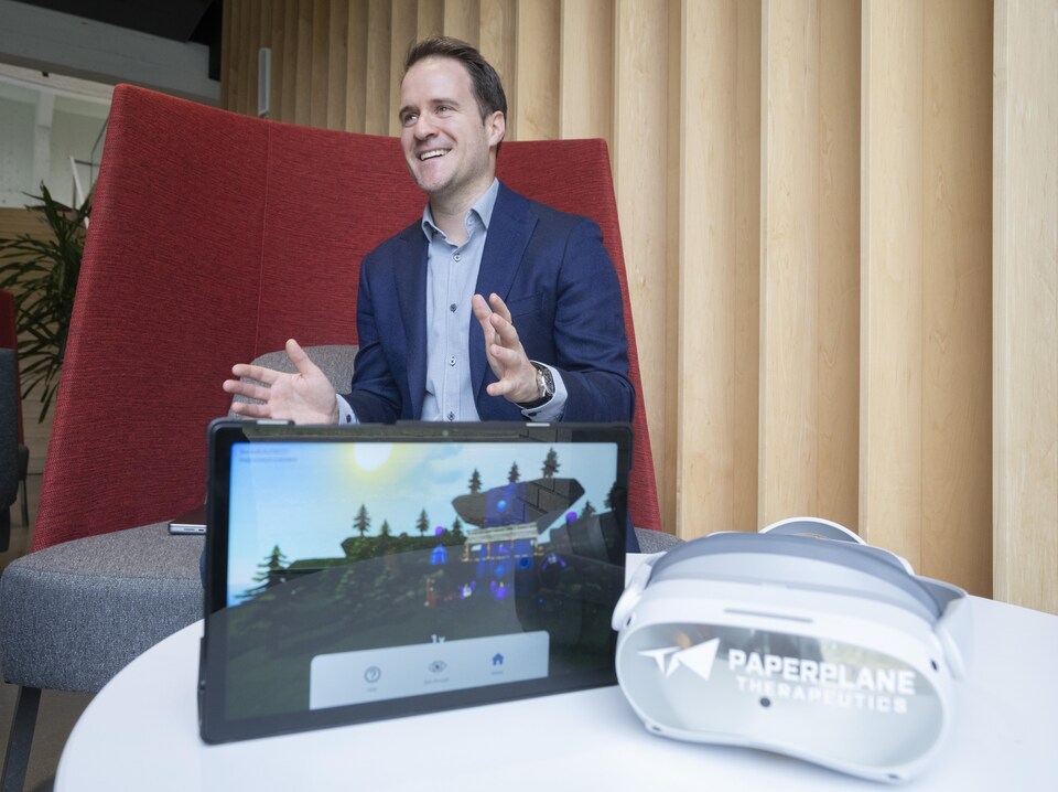 Le Dr Jean-Simon Fortin est assis sur un fauteuil derrière un casque de réalité virtuelle et une tablette qui affiche un jeu.