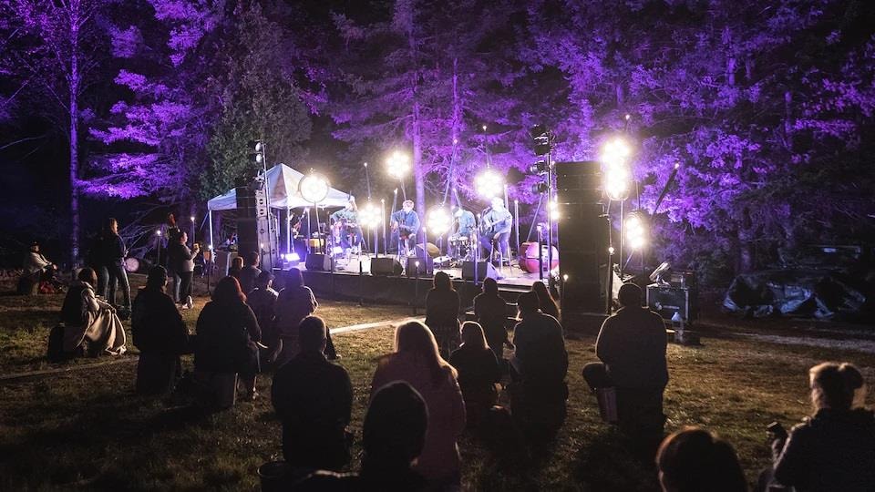 Un groupe en spectacle le soir, devant une foule en distanciation sociale.