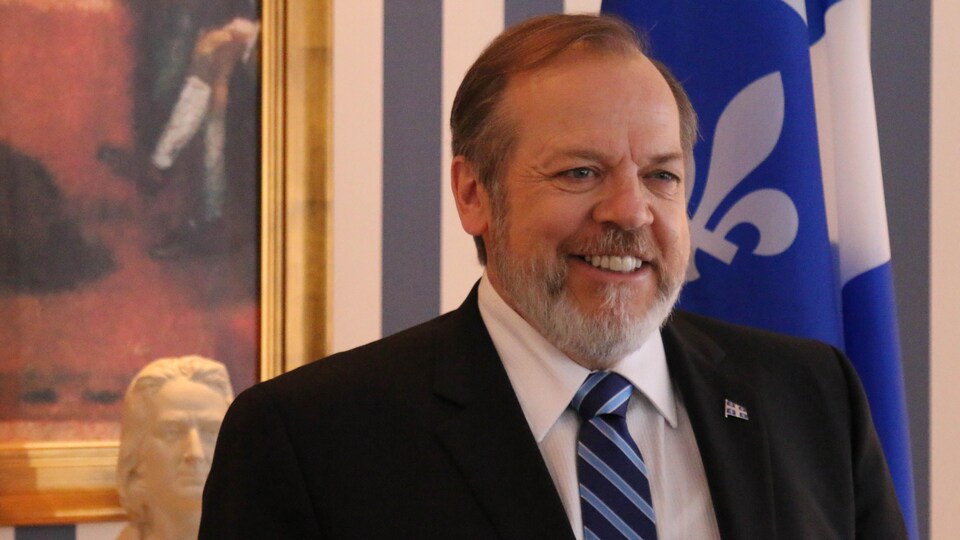 Portrait de l'homme devant un cadre et un drapeau du Québec.