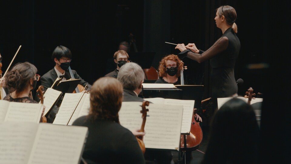 Une cheffe d'orchestre dirige des musiciens et musiciennes durant une répétition.