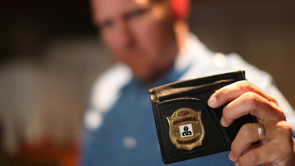 Un homme flouté montre son badge d'huissier. 