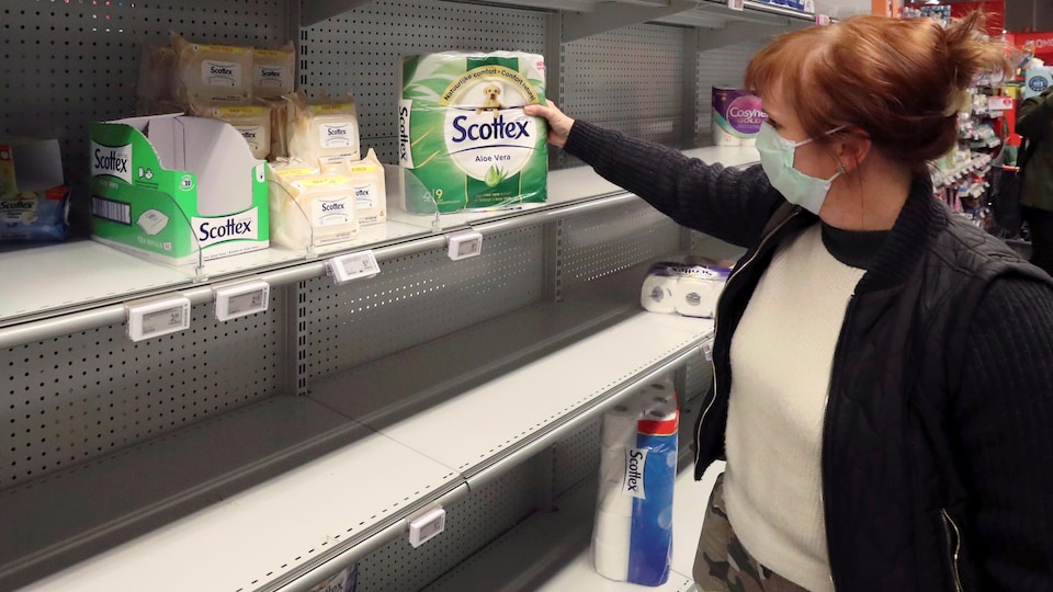 Une dame portant un masque achète l'un des dernier emballage de papiers de toilette.