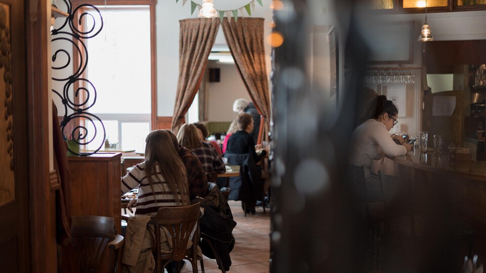 Des clients assis aux tables du restaurant et une autre cliente accoudée au bar près de la cuisine du Crêpe chignon.