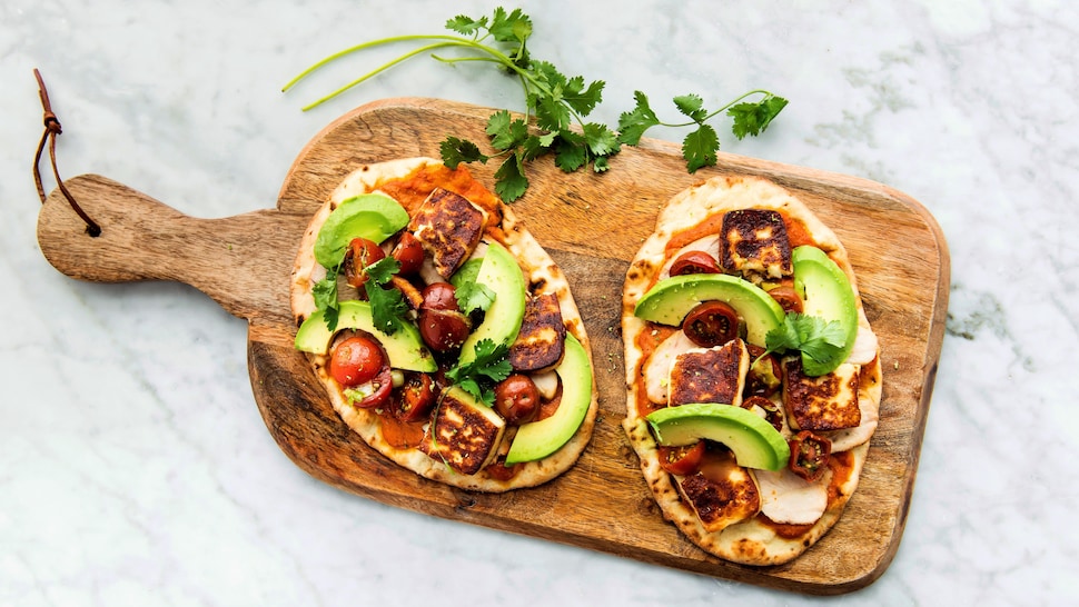 Deux pizzas au poulet sur pains naans se trouvant sur une planche en bois.
