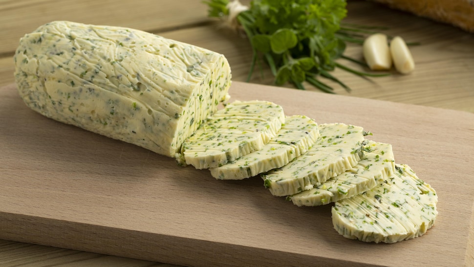 Un bloc de beurre aux herbes est découpé sur une planche de bois.