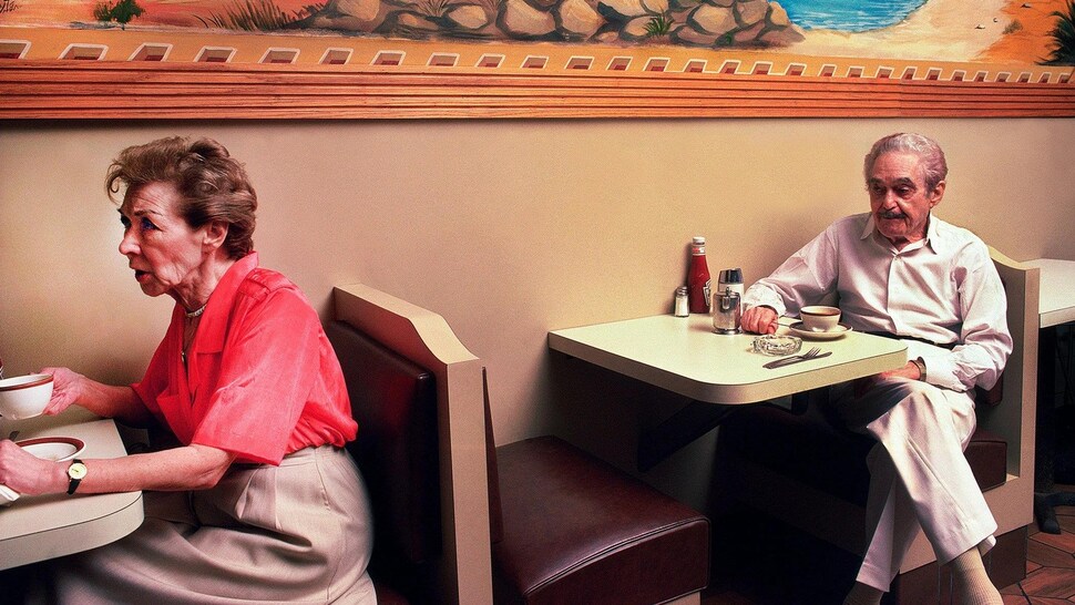 Un homme et une femme âgés mangent au restaurant à deux tables différentes. 
