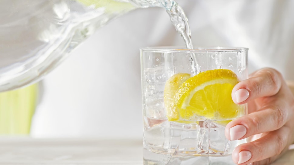 Une personne vers de l'eau dans un verre dans lequel il y a deux tranches de citron.