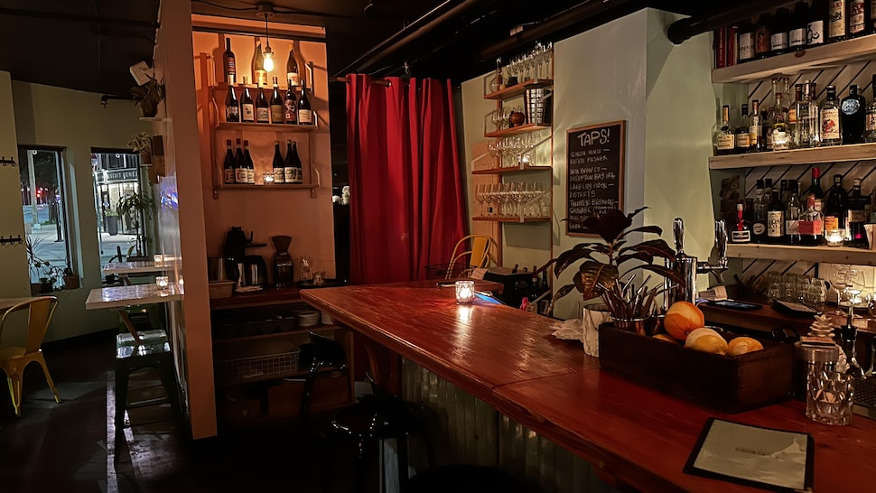 Un comptoir de bar dans les tons rouges, avec des bouteilles autour. 