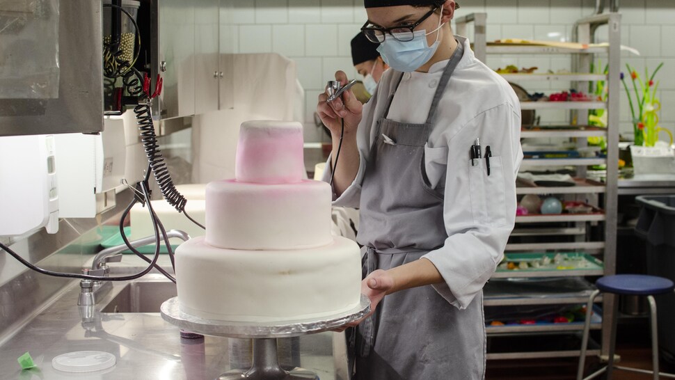 Un étudiant utilise un aérographe pour colorer son gâteau.