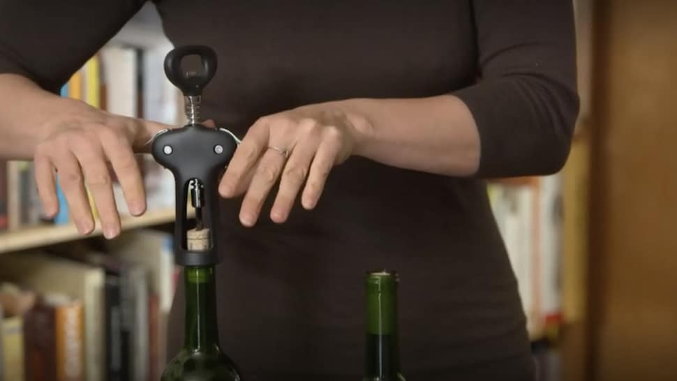 Une personne utilise un tire-bouchon pour ouvrir une bouteille de vin.