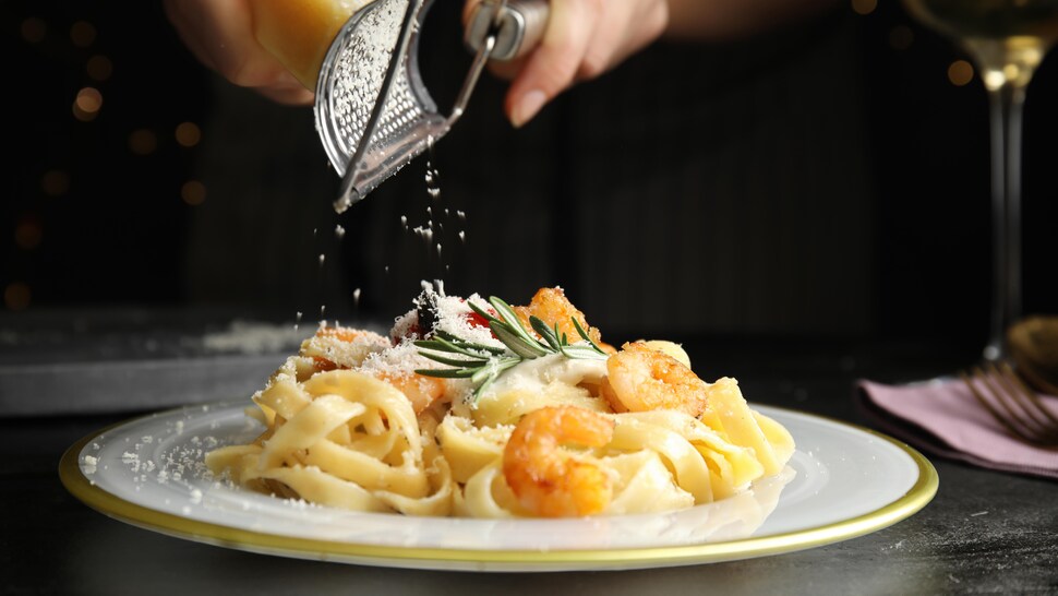 Une femme râpe du parmesan sur une assiette de linguines aux crevettes. 