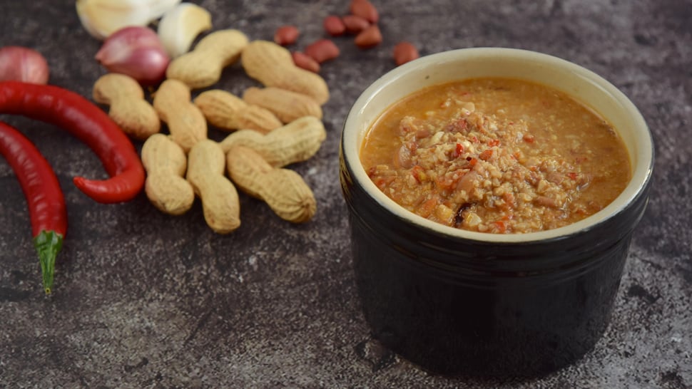 Un bol de marinade aux arachides sur un comptoir déposé à côté de piments, d'arachides et de gousses d'ail.