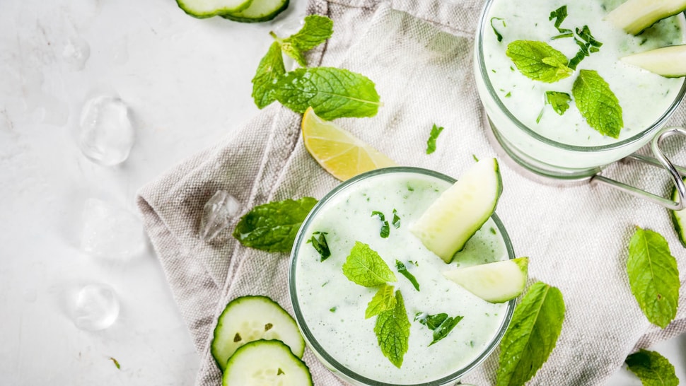Deux soupes blanches dans des tasses en vitre avec des morceaux de concombres, de lime et de la menthe.