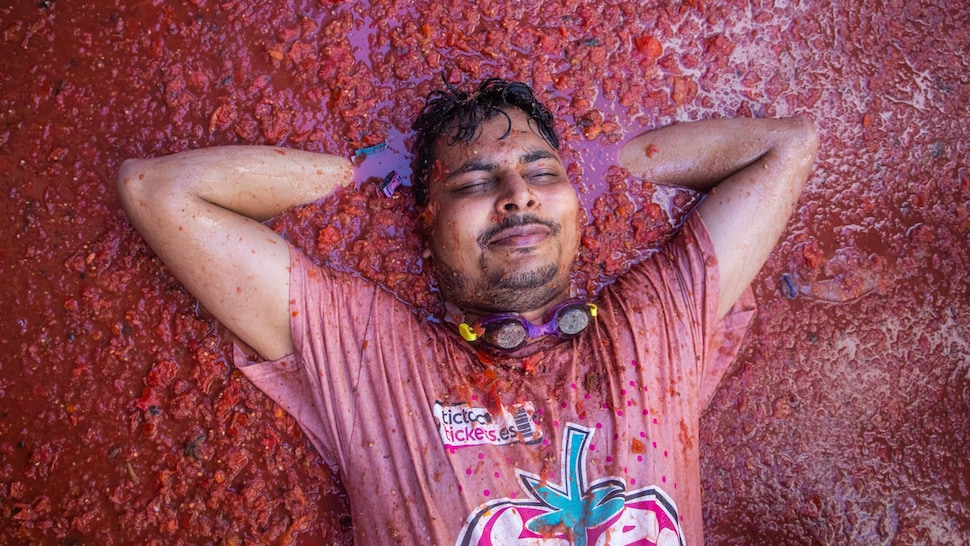 Une personne est couchée sur des tomates écrasées formant une épais liquide. 