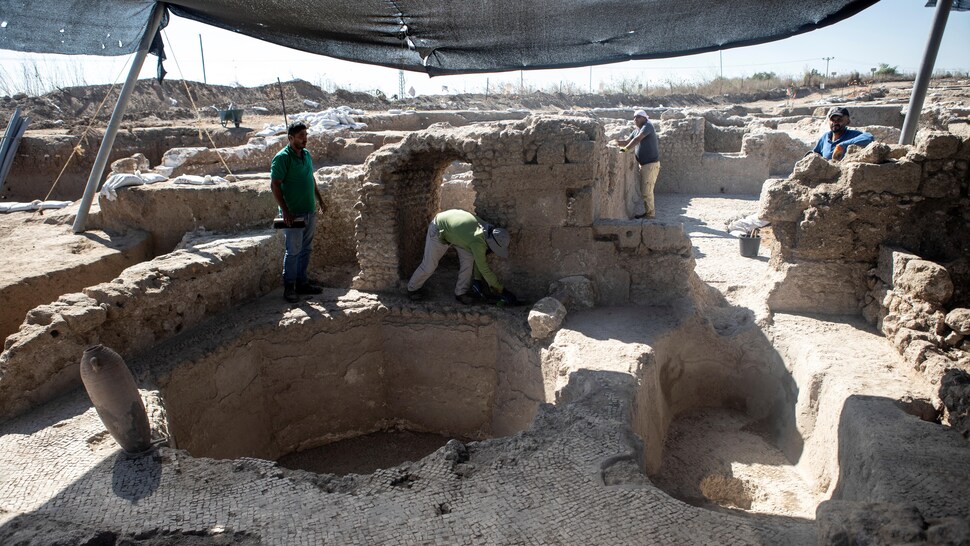 Des travailleurs nettoient le sol et les murs du site archéologique, sous une bâche.