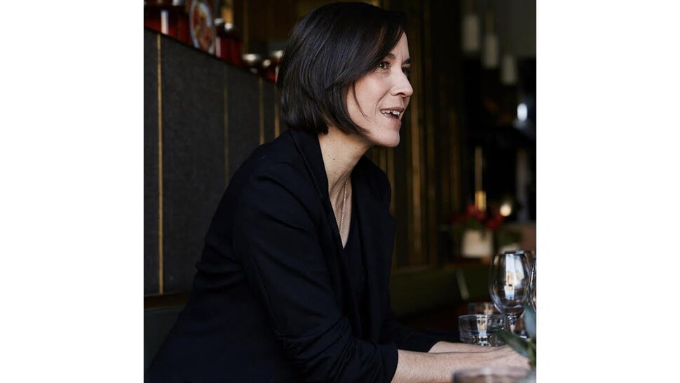 La sommelière Véronique Dalle est assise à la table d'un restaurant avec un verre de vin.