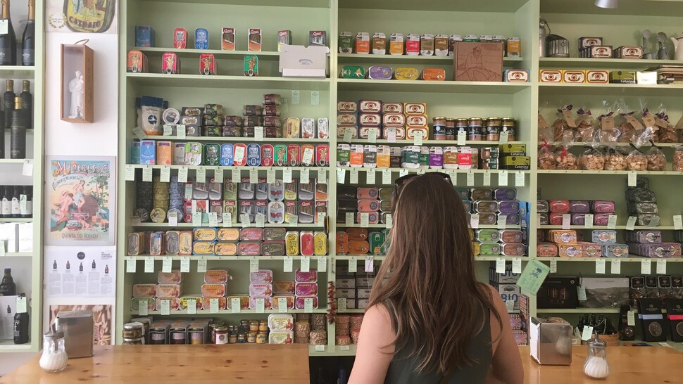 Dans une boutique un présentoir est rempli de conserve de sardines de différentes formes et de couleurs. 