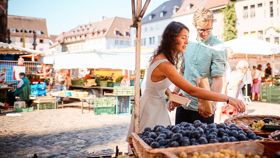 Une homme et une femme devant un kiosque de fruits dans un marché de producteurs.