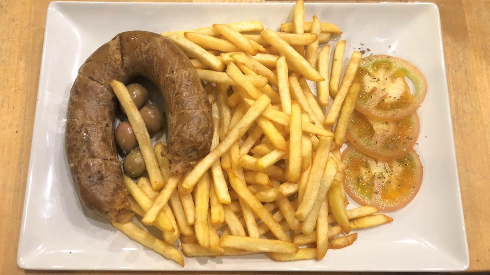 Une saucisse portugaise en forme de fer à cheval dans une assiette avec des olives, des frites et des tranches de tomates.