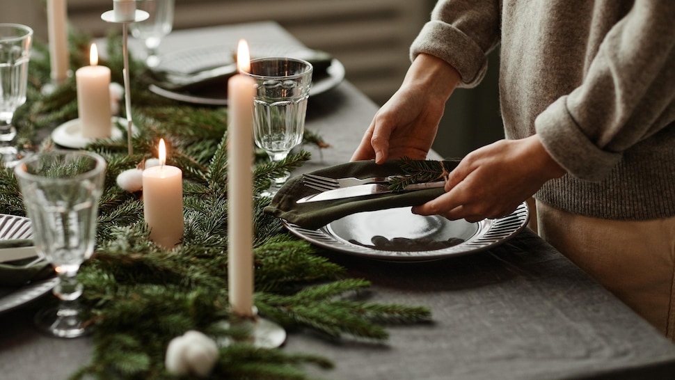 Une personne dépose ustensiles et vaisselles sur une table décorée pour Noël.
