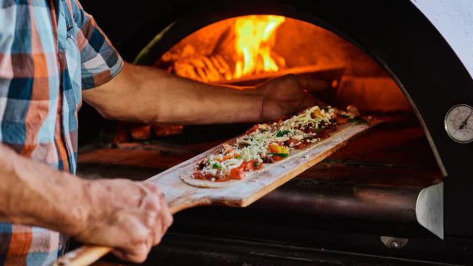 Un cuisinier s'apprête à mettre la pizza dans le four à bois. 