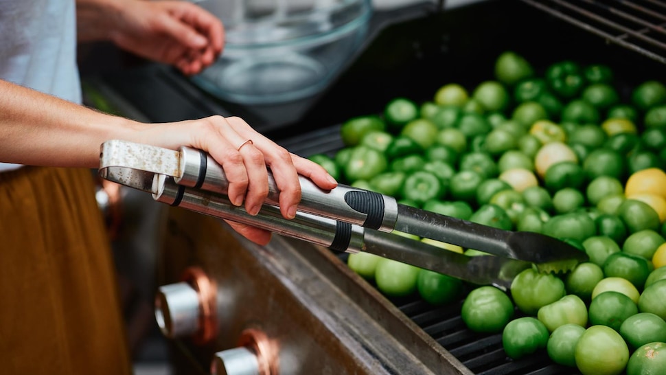 Femme qui tourne des tomates vertes sur un barbecue.