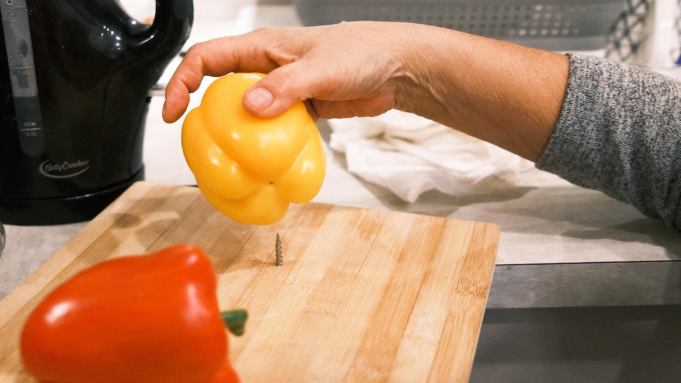 Une personne place un poivron sur une planche à découper munie d'une vis.