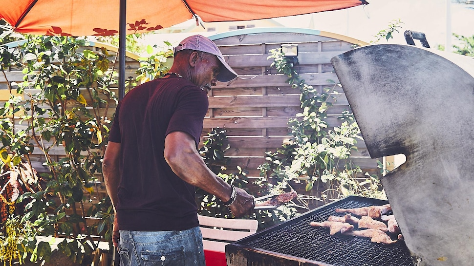 Martiniquais qui fait cuire de la viande sur un grill.